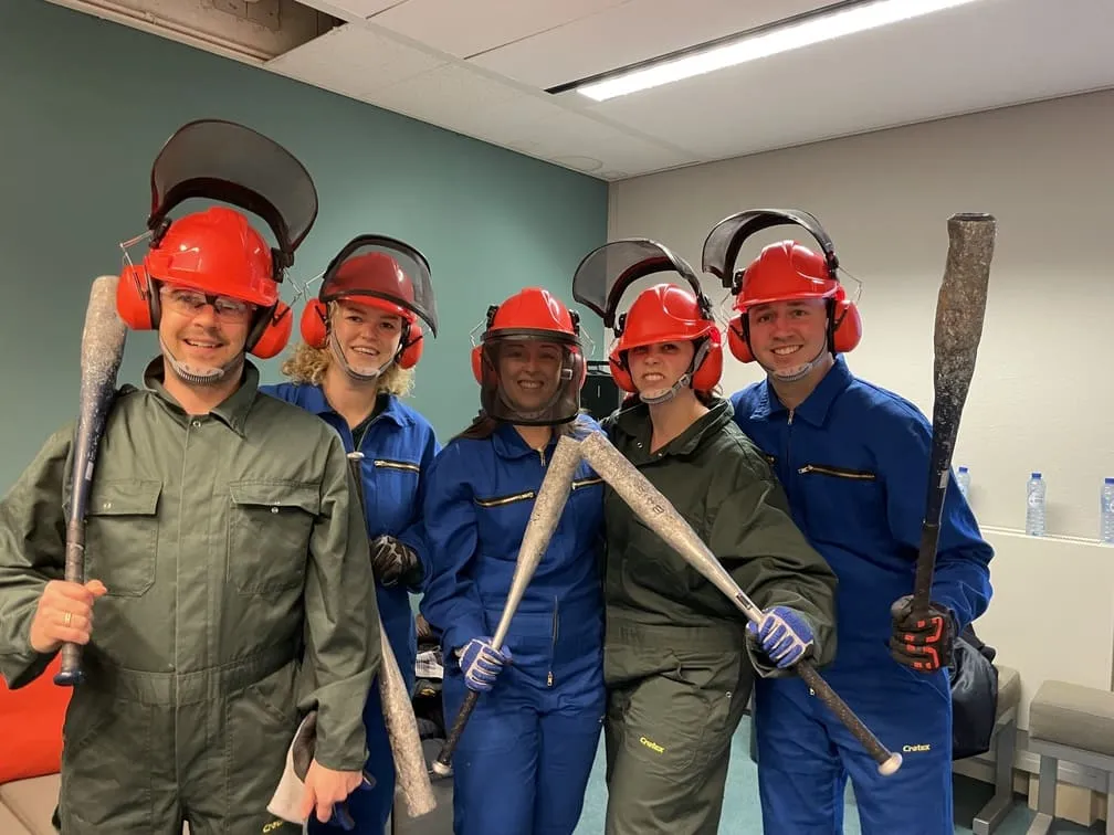 Rage room group in full safety gear holding bats, smiling together