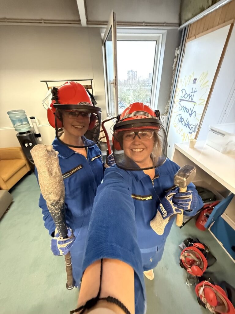 Two people smiling in rage room gear ready to smash
